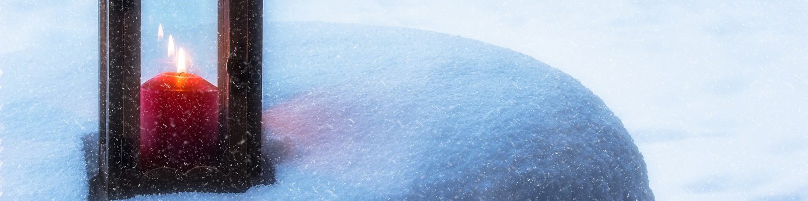 Rött blockljus i en ljuslykta placerad på snötäckt kulle.
